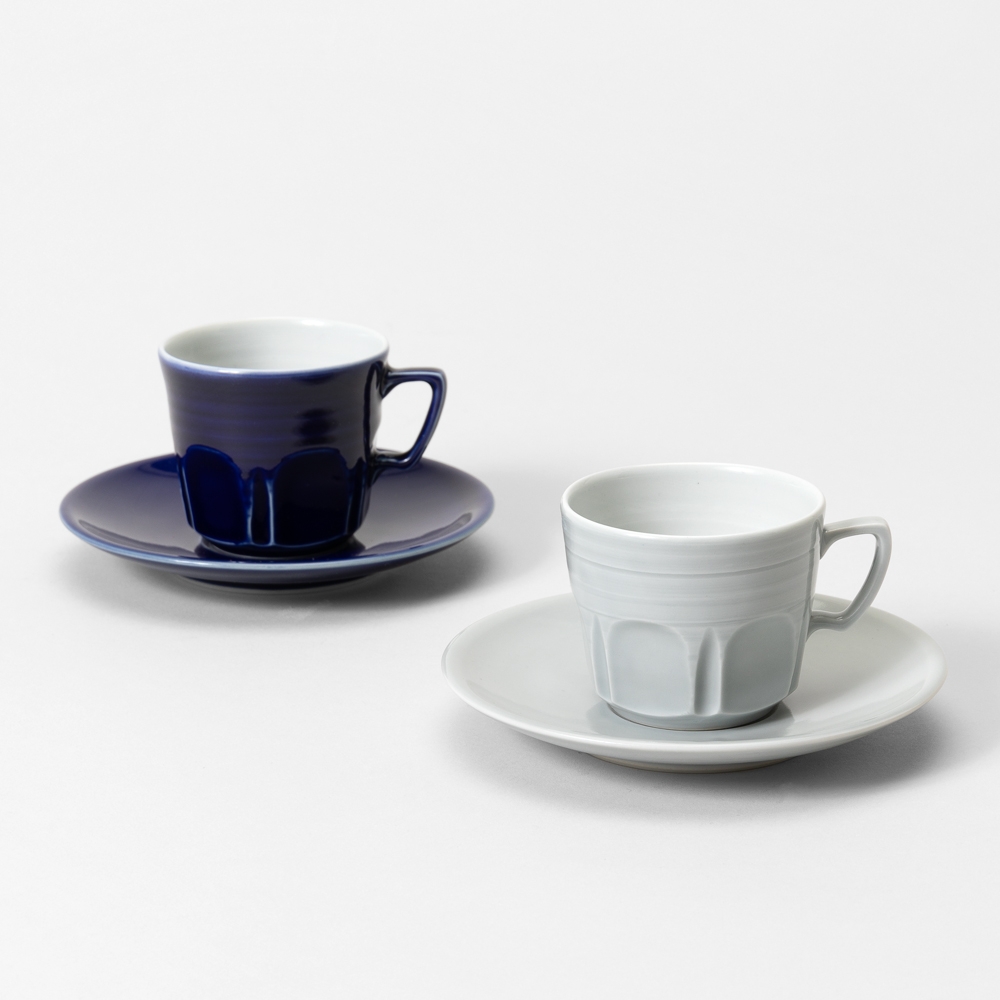 Two ceramic cups with matching saucers. One set is dark blue, the other is light gray.