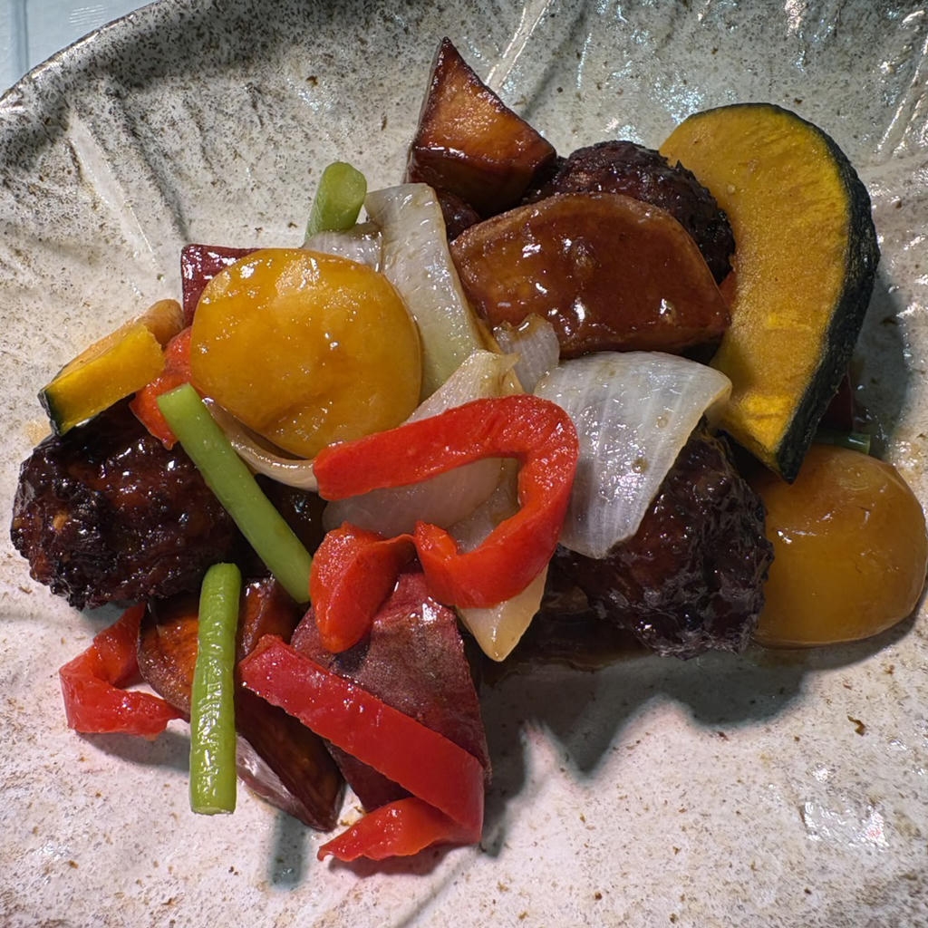 A ceramic plate with a colorful stir-fry of vegetables including red peppers, onions, green beans, potatoes, and squash slices.