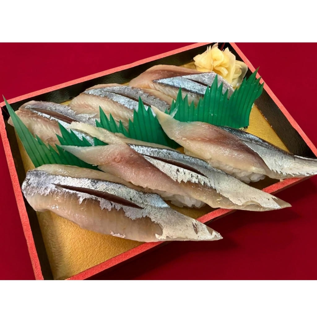 A neatly arranged sushi platter with six pieces of mackerel nigiri, garnished with green decorative leaves and pickled ginger.