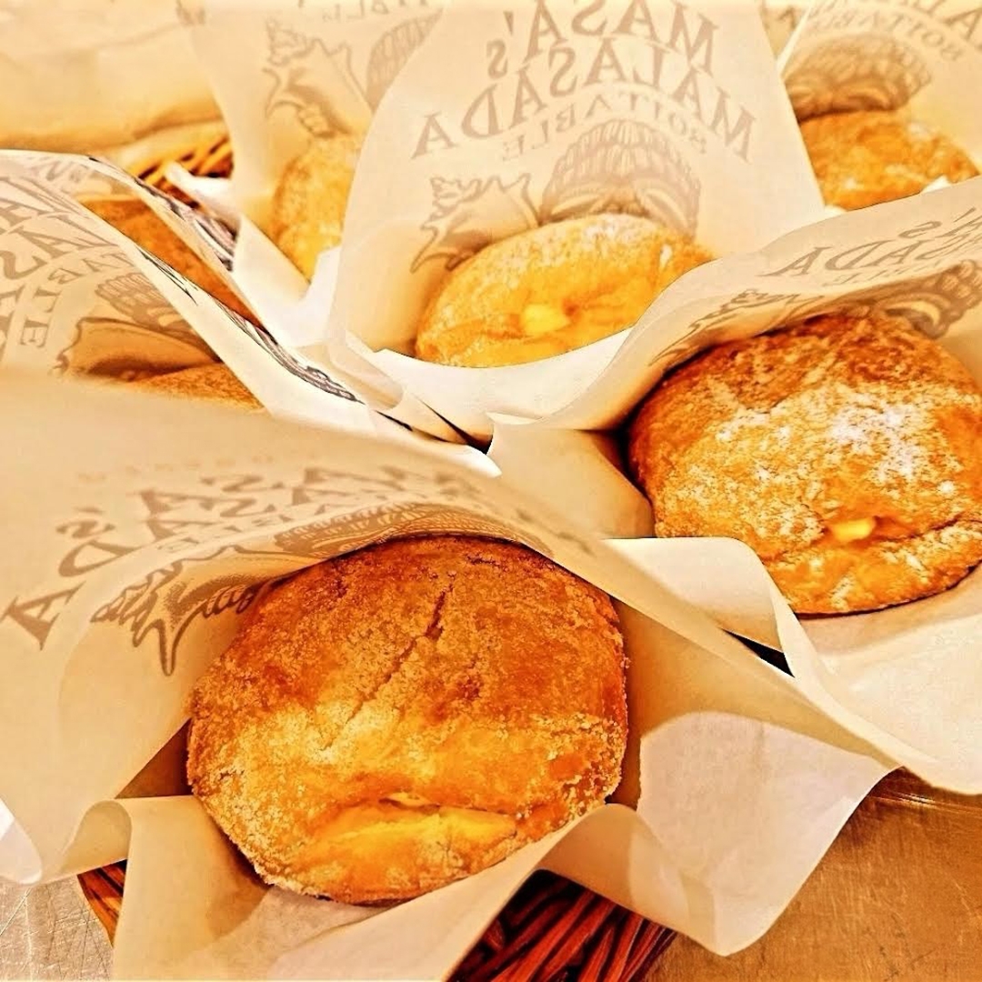 Breads wrapped in branded paper, displayed in a basket, with golden crusts and a dusting of flour.