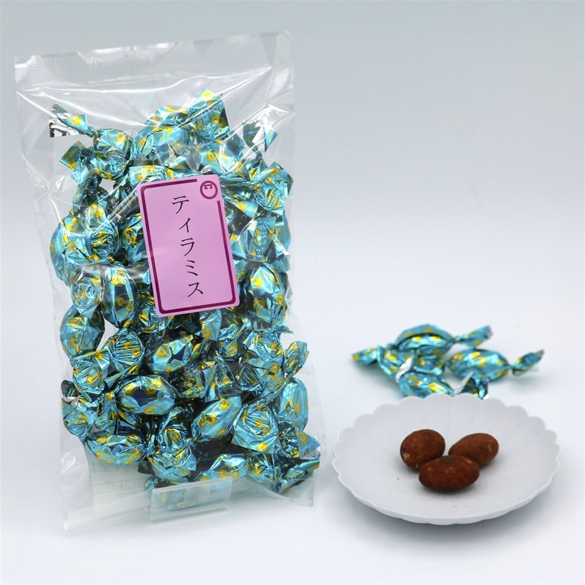 A bag of tiramisu-flavored candies wrapped in blue foil beside a small plate holding three unwrapped brown candies.