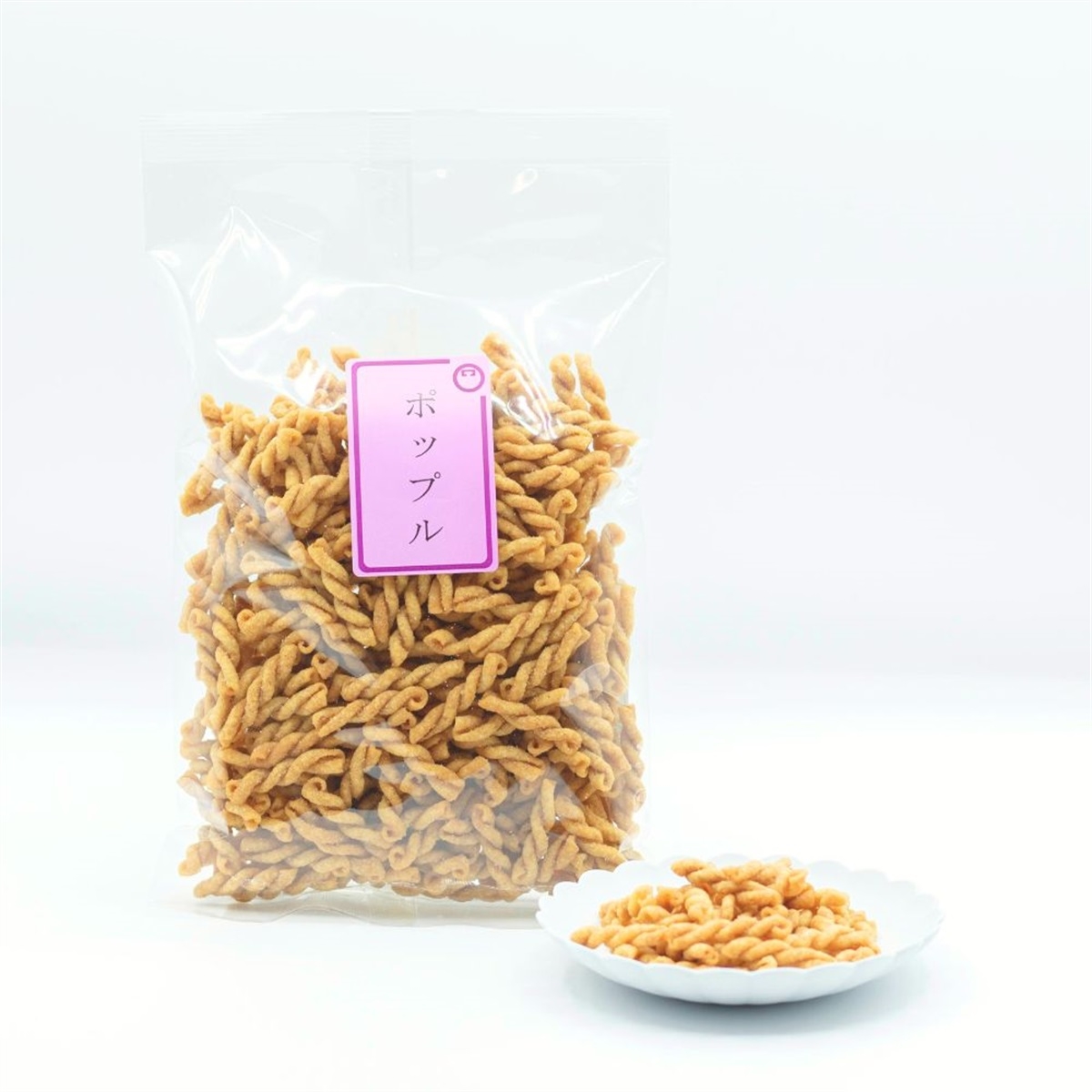 A clear bag and a small white plate filled with twisted, crunchy snacks. The bag has a pink label with Japanese text.