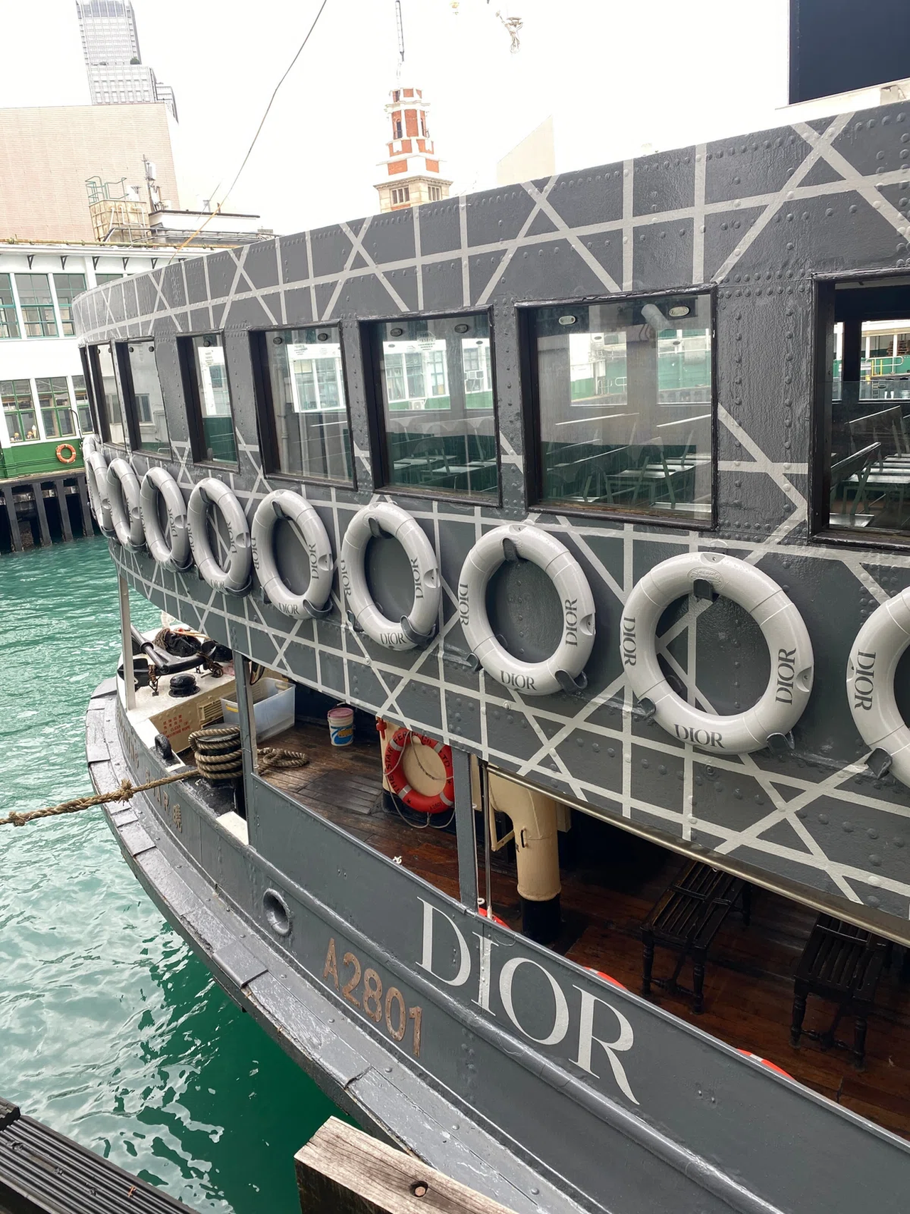 A Dior-branded boat docked, featuring lifebuoys with the Dior logo and a gray geometric pattern on its side.