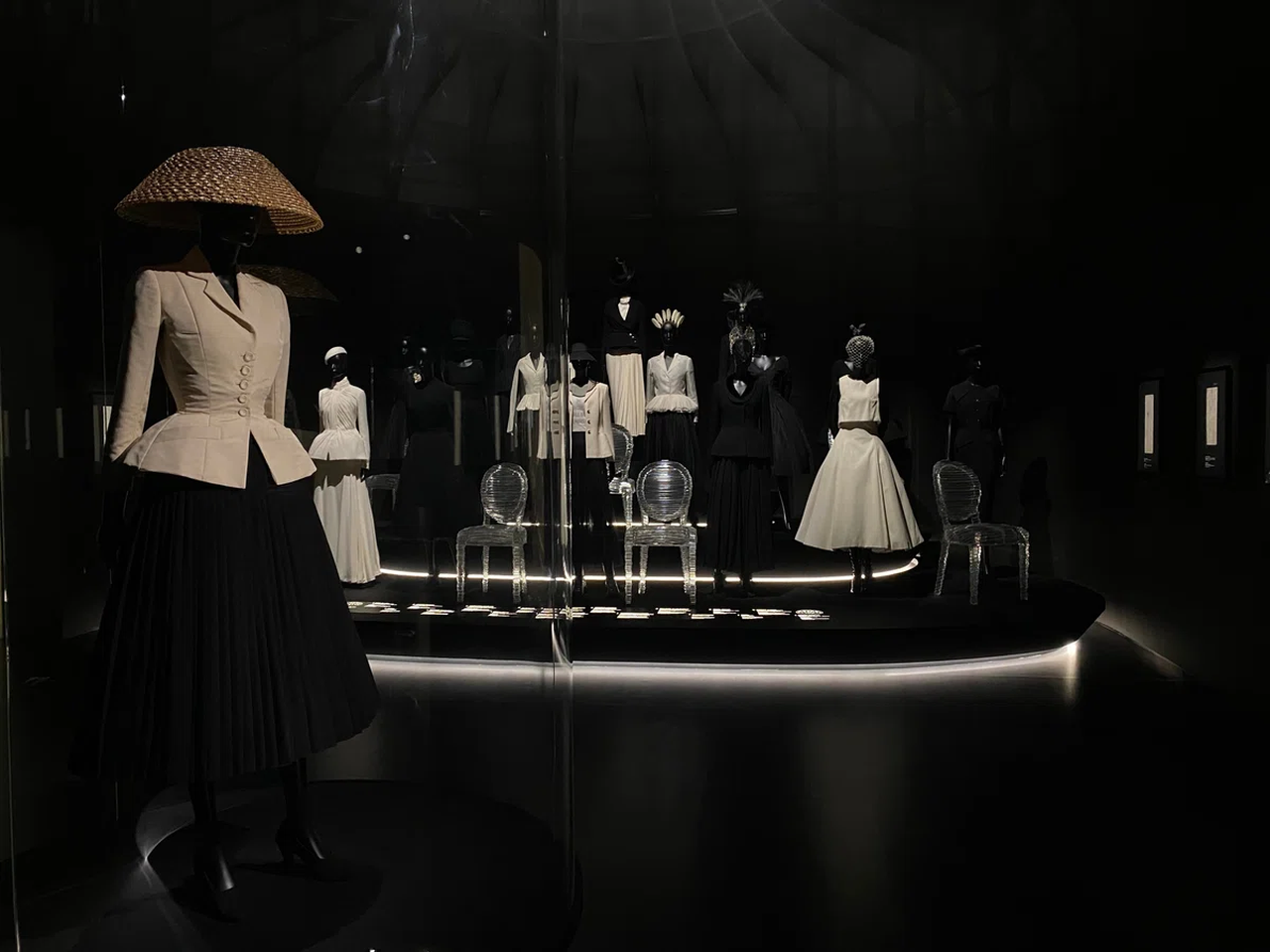 Exhibit of vintage black and white dresses on mannequins in a dimly lit room, featuring a hat and elegant gowns.