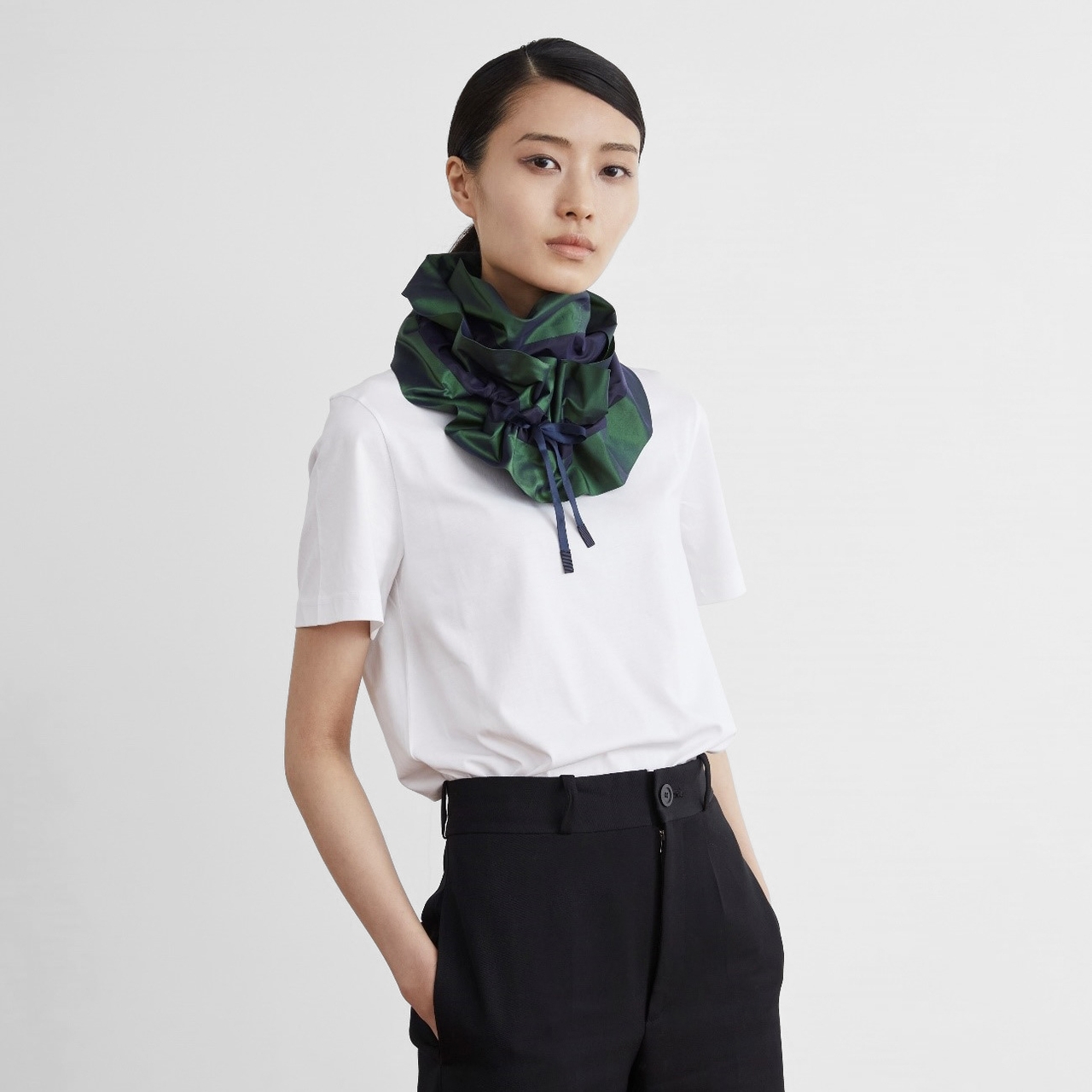 Person wearing a white T-shirt and black pants, with a green and blue patterned scarf around the neck.