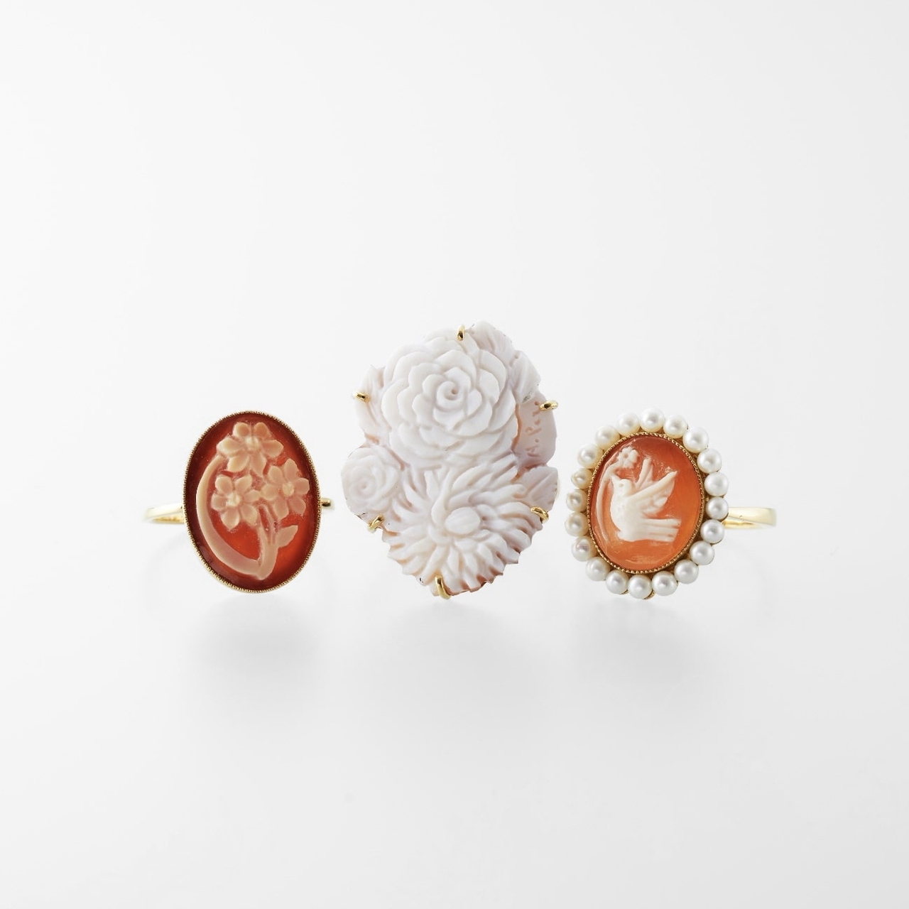 Three cameo rings: one with flowers, one with a white rose, and one with a bird surrounded by pearls.