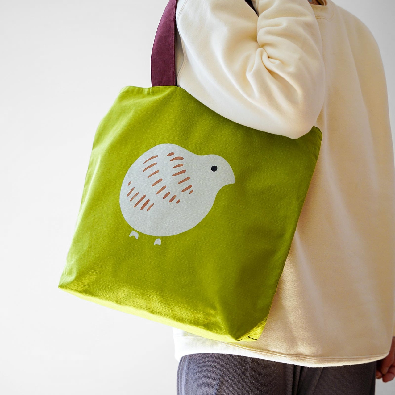 Person holding a green tote bag with a white bird design.