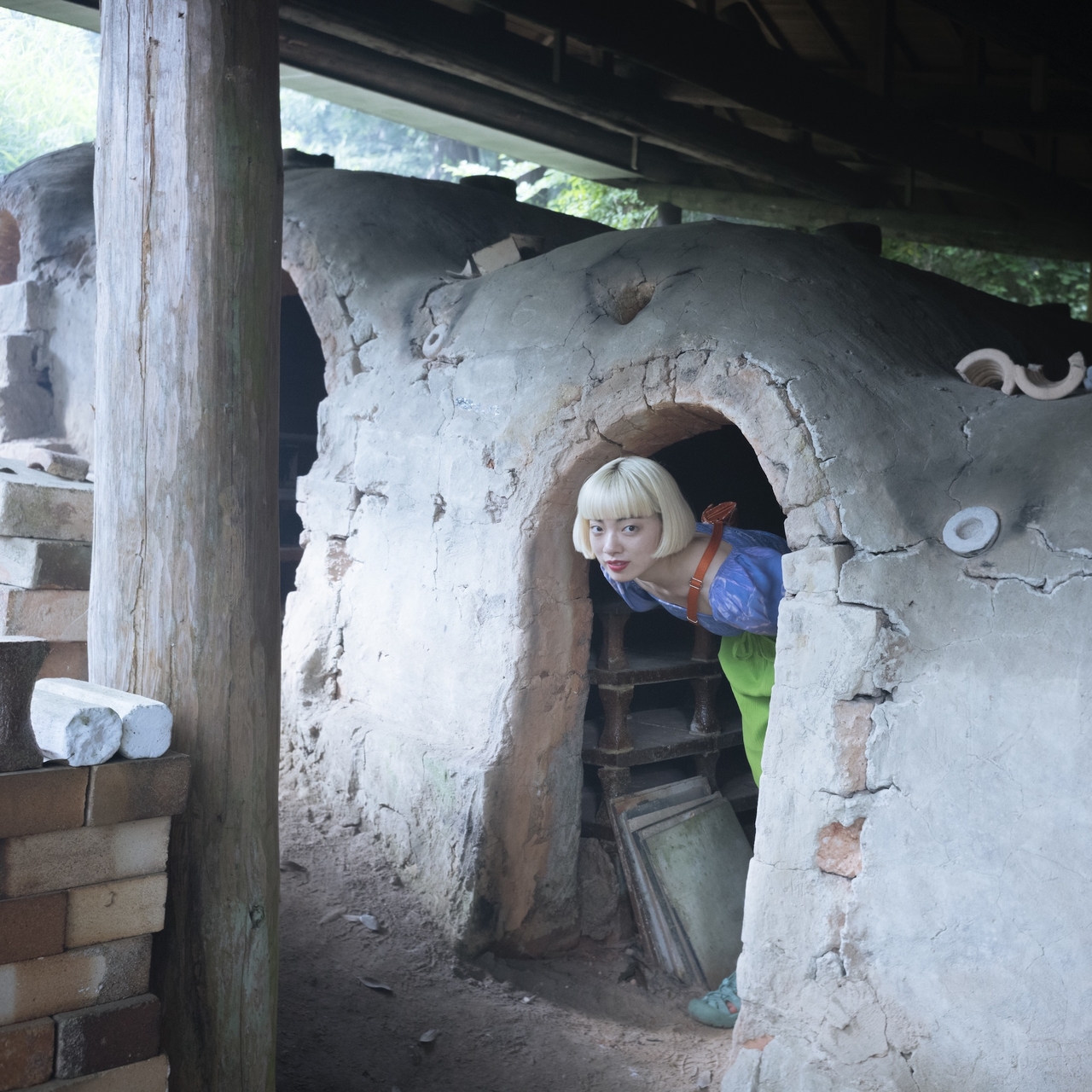 Person with blonde hair peeking out of a rustic clay oven, surrounded by bricks and wooden beams.