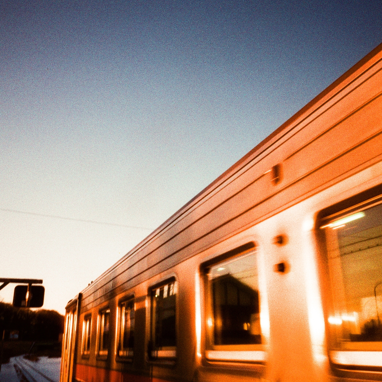 A train speeding past at sunset, reflecting warm orange hues, against a clear evening sky.