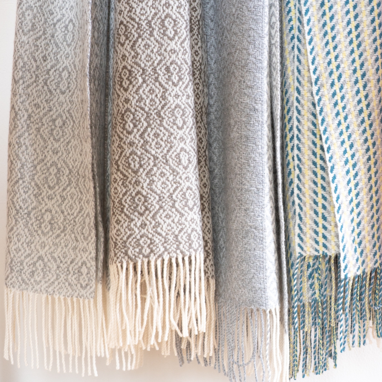 Hanging woven scarves with intricate patterns in gray, cream, and blue tones, featuring fringed edges.