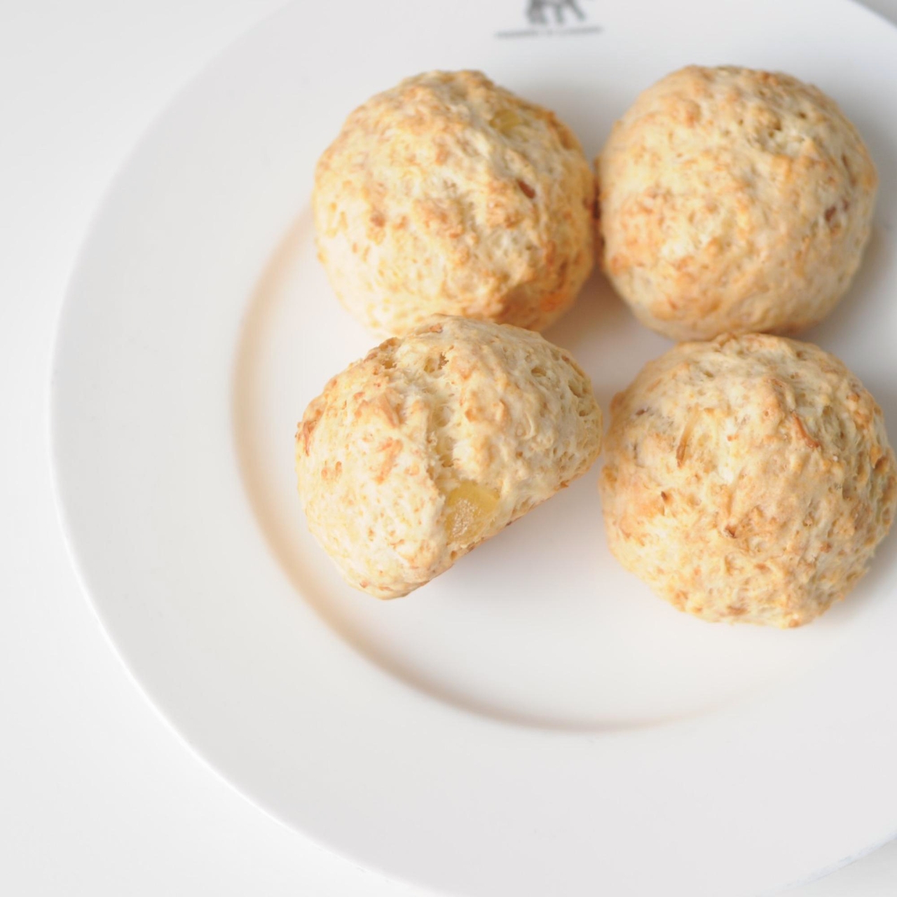 Four golden-brown scones on a white plate.