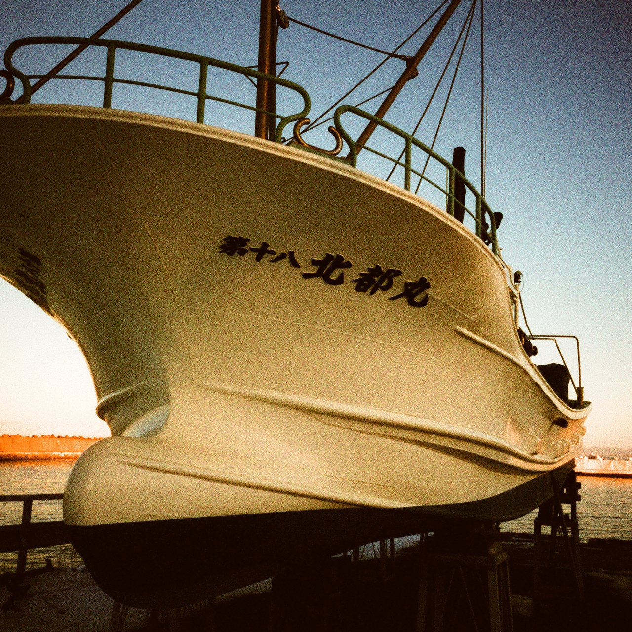 A large boat with Japanese text on its side is docked, viewed from a low angle against a clear blue sky.