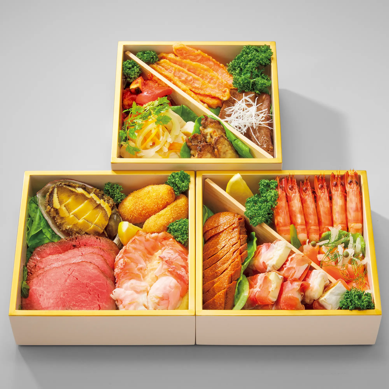 Three bento boxes filled with assorted Japanese dishes, including shrimp, sliced meat, seafood, vegetables, and garnishes.