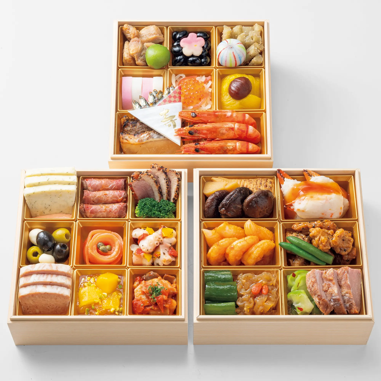Three wooden bento boxes filled with assorted colorful Japanese foods, including sushi, shrimp, vegetables, and decorated desserts.