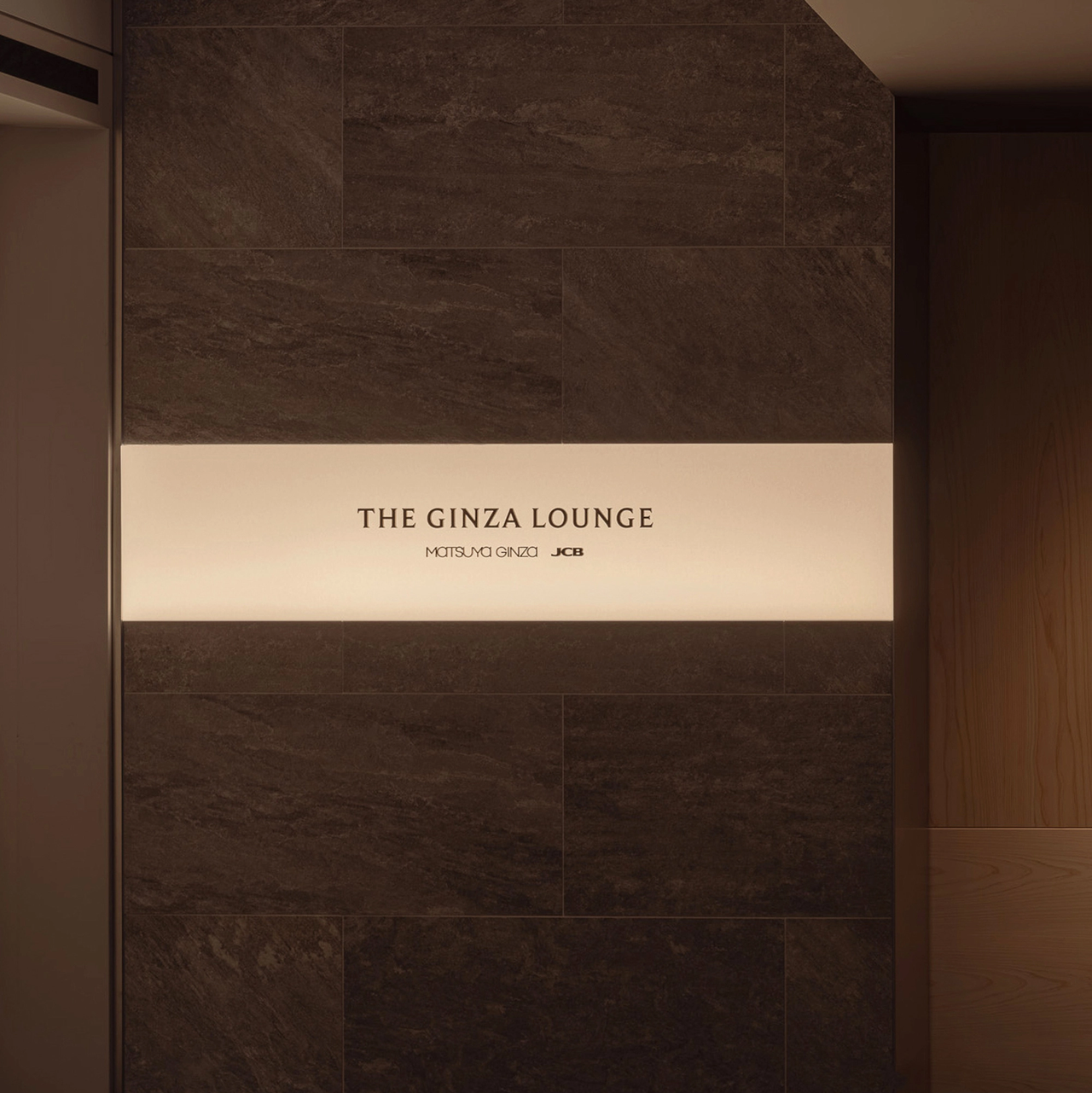 暗い壁に掲げられた発光サインには「The Ginza Lounge, Matsuya Ginza, JCB」と記され、モダンで洗練された雰囲気を演出しています。