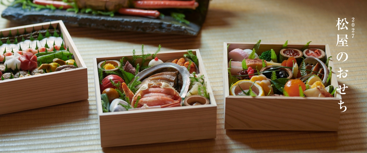 木製のテーブルの上に、色とりどりの魚介類や野菜が盛り付けられた、伝統的な日本のおせちの重箱が並んでいる。側面には「2027松屋のおせち」のロゴ。