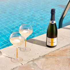 Two glasses of champagne and Veuve Clicquot Rich on Ice bottle on the edge of a pool with blue tiles, creating a luxurious and refreshing scene.