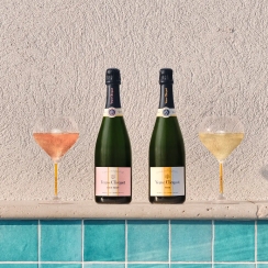Two bottles of champagne, Veuve Clicquot Rich on Ice and Veuve Clicquot Rich on Ice Rosé&nbsp; with matching filled glasses, placed on the edge of a pool with a textured wall backdrop.