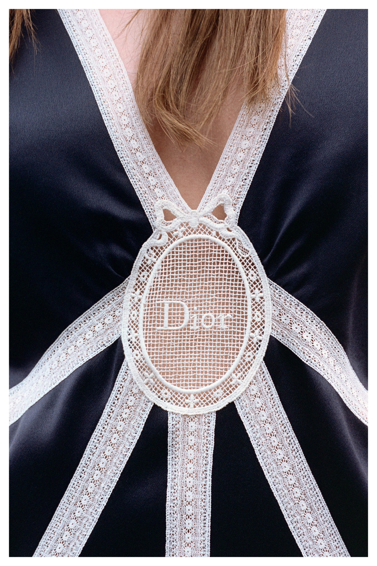 Close-up of a black Dior garment featuring a central lace embellishment with "Dior" text, and intersecting white lace strips.