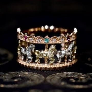 A detailed carousel-themed ring featuring miniature horses and intricate designs, adorned with small colorful gemstones.