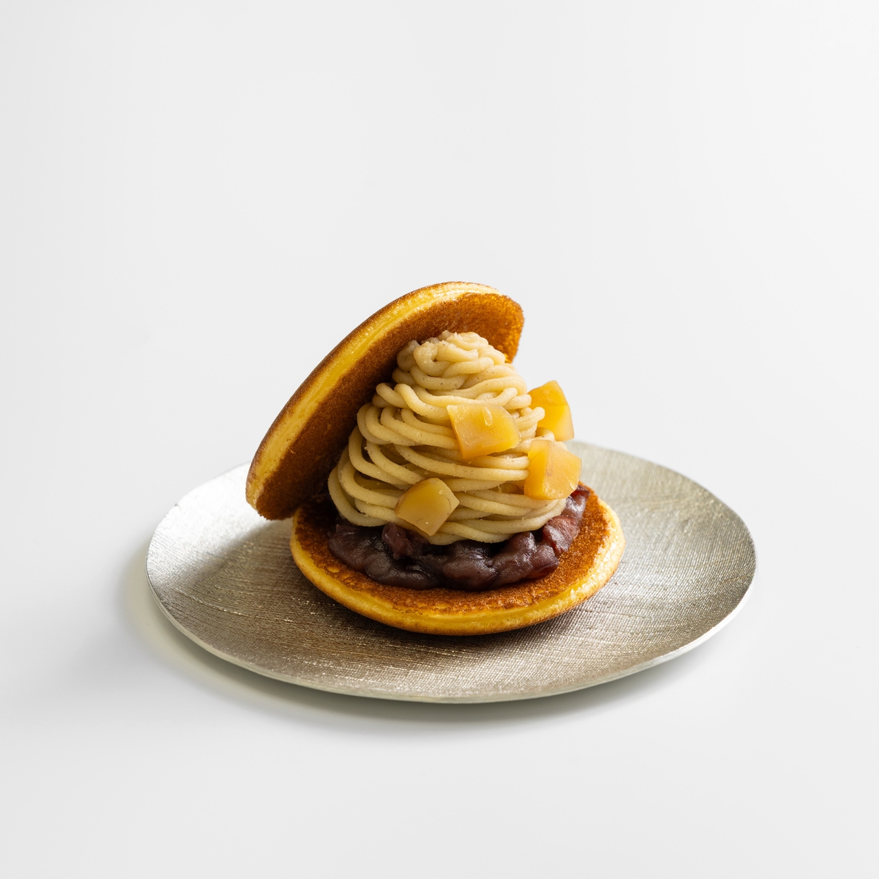 A dessert with two pancakes, filled with red bean paste, chestnut cream, and diced chestnuts on a silver plate.