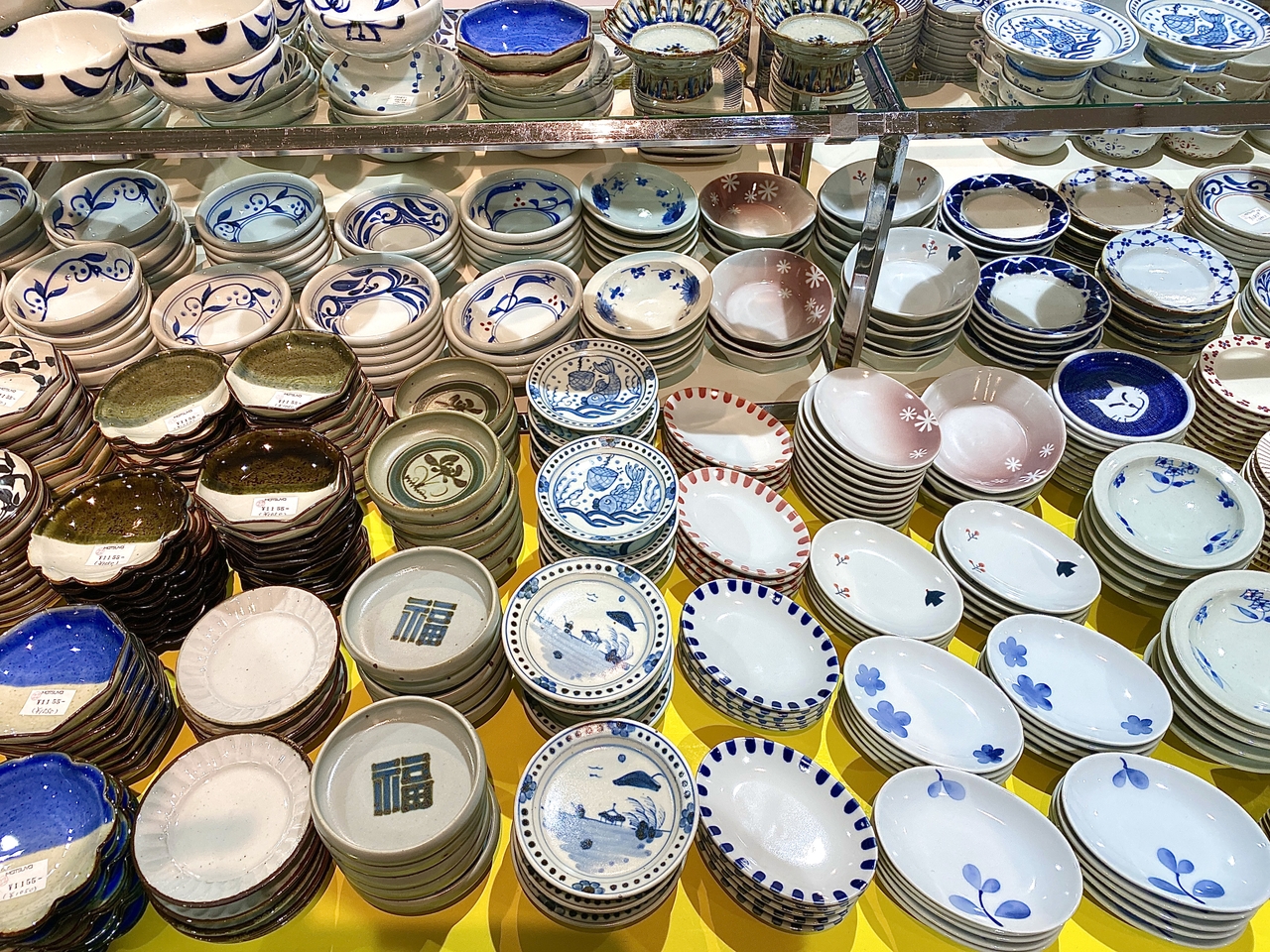 Assorted stacks of decorative ceramic plates and bowls with various patterns, displayed on shelves in a store.