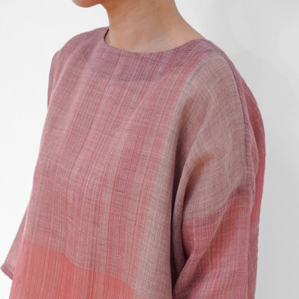 Person wearing a loose-fitting, textured pink and beige gradient top.