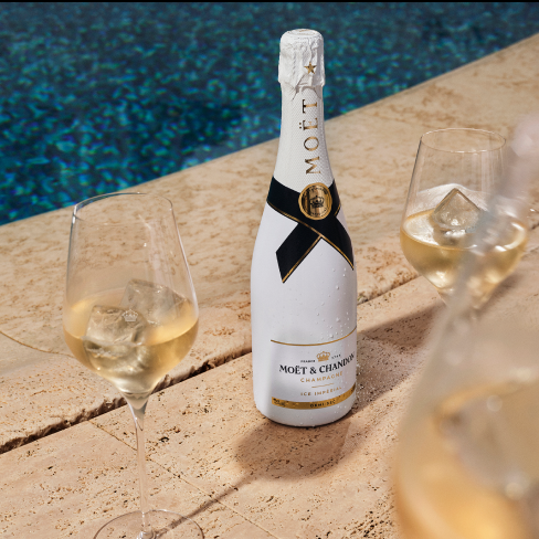 A bottle of Moët & Chandon champagne, Moët & Chandon Ice Impérial  with three filled glasses sits on a stone surface by a pool.