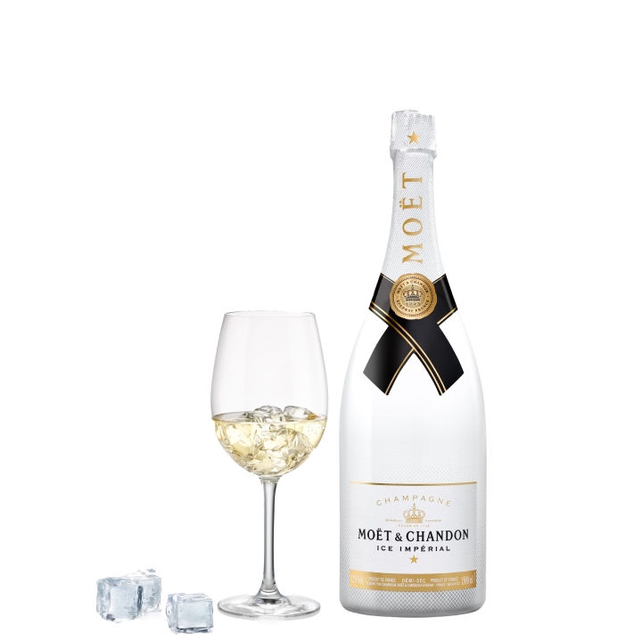 A bottle of Moët & Chandon Ice Impérial champagne next to a glass filled with the champagne and ice cubes, with additional ice cubes nearby.