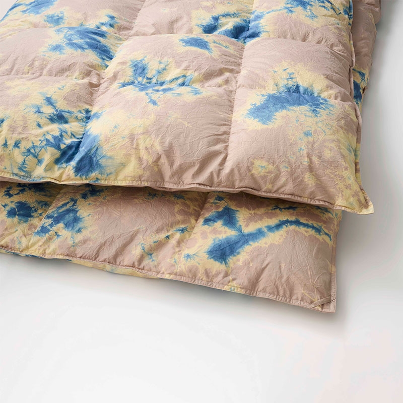 A folded quilt with a tie-dye pattern in blue and yellow on a beige background, placed on a light surface.